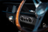 Close-up of a vintage car dashboard featuring a wood-rimmed steering wheel, chrome controls, and a black console panel.