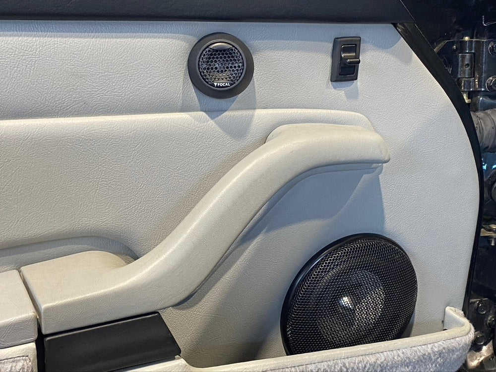 A car interior of a classic sports car in grey leather showing speakers and door handle